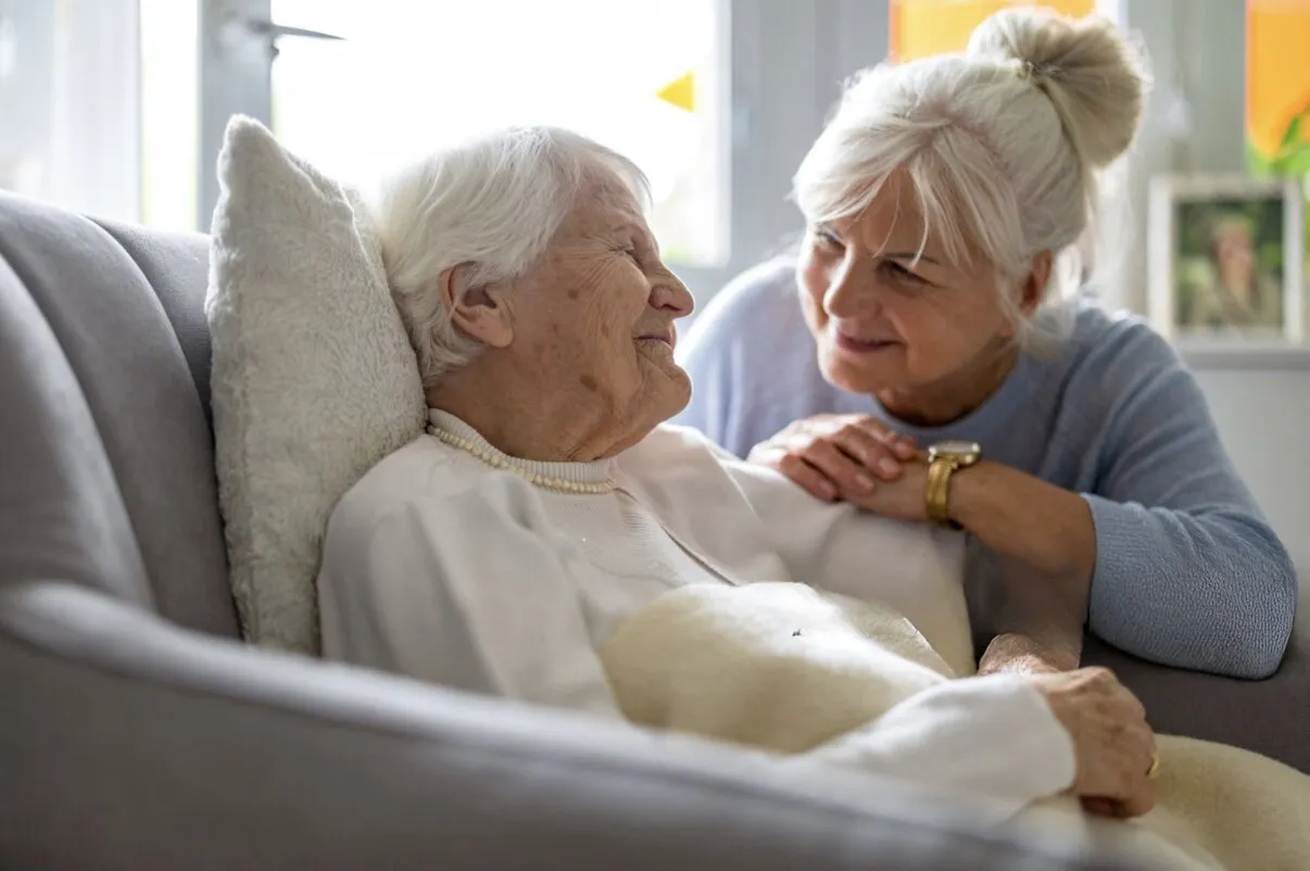 An older woman resting in an armchair while her daughter leans in beside her
